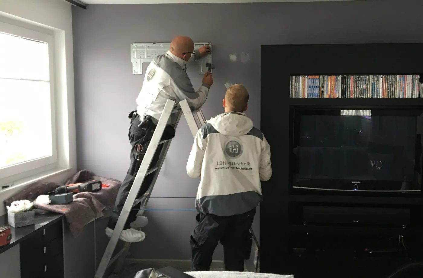 Zwei Monteure bei der Montage einer Klimaanlage in einem Wohnzimmer